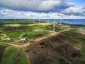 Aerial view of stormy clouds above wind turbines and pastures on ocean shore.