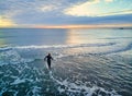 Aerial view swimmer with wetsuit and cap entering the sea water at sunrise