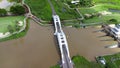 Aerial view of Tha Chomphu White Bridge, Lamphun, Thailand with river, forest trees and green mountain hill. An old railway bridge
