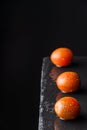 Aerial view of three wet and lined kumato cherry tomatoes, with selective focus, on black slate and black background vertically Royalty Free Stock Photo