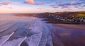 Aerial view of the town of Woolacombe and it`s beach at dawn, waves breaking on a beach, the headland of Morte Point bathed in