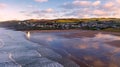 Aerial view of the town of Woolacombe and it`s beach at dawn, waves breaking on a beach, the sunlit clouds reflected in the