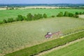 Aerial view on a tractor that collects hay in rows with a disc rake. Farmer stores fodder for cattle in summer season.