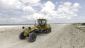 Aerial view of a tractor moving along the sand sea shore on blue cloudy sky background. Shot. Machine driving on beach. Royalty Free Stock Photo