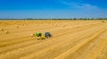 Aerial view of tractor tow trailed bale machine to collect straw from harvested field