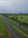 Aerial view of a tree-lined highway leading to a vast expanse of green grass in the distance Royalty Free Stock Photo