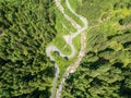 Aerial view of twisty road in the Alps with a small river and Bridge. Trees and road seen from top down. Strong green colors