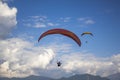 A aerial view of two pargliders on red yellow parachutes flying in a blue sky with white clouds over the mountains Royalty Free Stock Photo