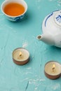 Aerial view of two scented white candles, teapot and blue cup with tea, on blue table, with selective focus, in vertical Royalty Free Stock Photo