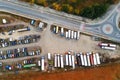 Aerial view of unpaved natural parking with lots of trucks, trailers and cars. Rest place near road and circle junction