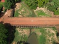 Aerial view of a rural unpaved road, crossing a quaint bridge in a lush forestry