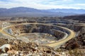 An aerial view of a vast open-pit mine with spiraling roads in a desert, framed by distant mountains under a clear sky