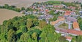 Aerial view of a village next to agricultural land behind a piece of forest with deciduous trees