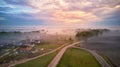 Aerial view of village, rural dirt road and trees covered by fog. Early misty morning sunrise panorama Royalty Free Stock Photo