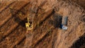 Aerial view of a wheel loader excavator with a backhoe loading sand onto a heavy earthmover at a construction site