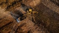 Aerial view of a wheel loader excavator with a backhoe loading sand onto a heavy earthmover at a construction site