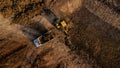 Aerial view of a wheel loader excavator with a backhoe loading sand onto a heavy earthmover at a construction site