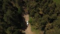 Aerial view. White car moving on dirt road on deepening into wooded area