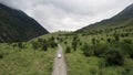 Aerial view of a white car moving on mountain rural road along wilderness. Action. Car driving on straight road during