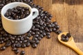 Aerial view of white cup with roasted coffee beans, wooden spoon, on wooden table Royalty Free Stock Photo