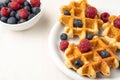 Aerial view of white plate with waffles with raspberries and blueberries, bowl with raspberries and blueberries, selective focus