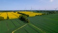 Aerial view Wind turbine on grassy yellow farm canola field against cloudy blue sky in rural area. Offshore windmill Royalty Free Stock Photo