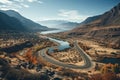 Aerial view of winding paved serpentine road next to river in scenic autumn mountains