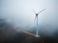 Aerial view of a windmill on the slope of the mountain on a foggy day