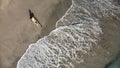 Aerial view of a woman in glow bikini sit on black sand beach taking photo of the sea in sunset. Royalty Free Stock Photo