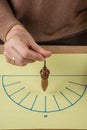 Aerial view of a woman`s hand holding a wooden pendulum over a yellow energy diagram, Royalty Free Stock Photo