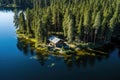 Aerial view of a wooden house on the shore of the lake. Aerial view of wooden cottage in green pine forest by the blue lake in