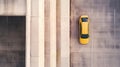 Aerial view of a yellow car parked in an empty parking lot next to a large concrete structure