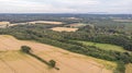 An aerial view of a yellow crop field with traces of tractor, trees and forest under a majestic stormy sky