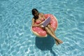 Aerial view of a young brunette woman swimming on an inflatable big donut with a laptop in a transparent turquoise pool. Royalty Free Stock Photo