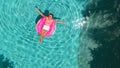 Aerial view of a young brunette woman swimming on an inflatable big donut with a laptop in a transparent turquoise pool. Royalty Free Stock Photo