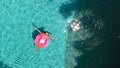 Aerial view of a young brunette woman swimming on an inflatable big donut with a laptop in a transparent turquoise pool. Royalty Free Stock Photo
