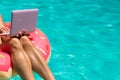 Aerial view of a young brunette woman swimming on an inflatable big donut with a laptop in a transparent turquoise pool