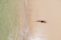 Aerial view of young woman in black bikini lying on beach with white sand, foaming waves of the Indian Ocean. Bali Island,