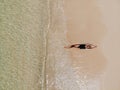 Aerial view of young woman in black bikini lying on beach with white sand, foaming waves of the Indian Ocean. Bali Island, Royalty Free Stock Photo