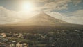 Aerial volcano erupt at sunlight closeup. Sun cityscape of rural town at green volcano valley