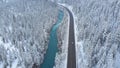 AERIAL: White car drives down empty road running along the river in the winter. Royalty Free Stock Photo