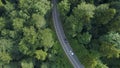 AERIAL: White car trailing dark car down empty road leading through the forest. Royalty Free Stock Photo