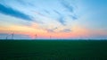 Aerial wide shot of wind farm beyond green farmland on gorgeous sunset evening