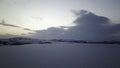 Aerial winter panoramic view of frozen lake surrounded by hills covered by trees and snow on sunset cloudy sky Royalty Free Stock Photo