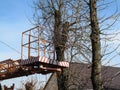 Aerial work platform against the backdrop of bare autumn-spring-winter trees, roof and blue sky, nobody. Pollarding trees in the Royalty Free Stock Photo