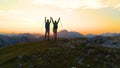 AERIAL: Young hiker couple outstretch their arms as they catch the sunset. Royalty Free Stock Photo