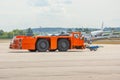 Aerodrome orange tow tractor is driving along the steering paths at the airport