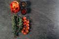 An aesthetic arrangement of sprigs of fragrant rosemary, three rings of red pepper, a branch of cherry tomatoes and two black cups Royalty Free Stock Photo