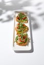 Aesthetic composition with shrimp bruschetta on white background with shadows from flowers. Italian bruschetta with shrimp,