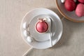 Aesthetic Easter holiday table setting, pink colored egg in cup with bunny ears, on white plates, spoon, small candies